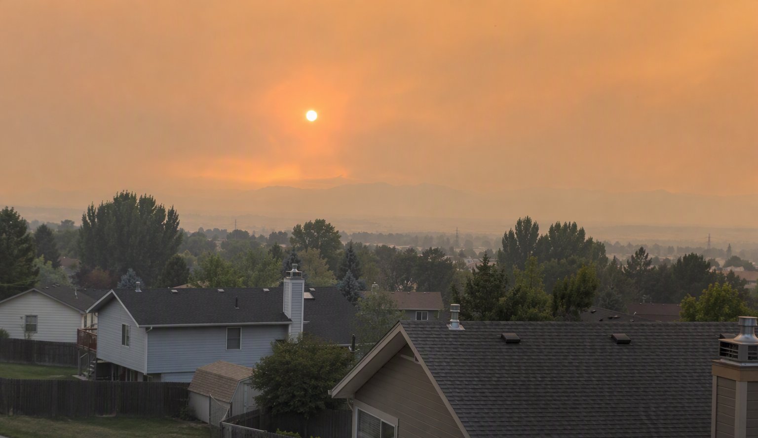 Suburban rooftops under an orange wildfire smoke haze